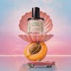 Perfume bottle labeled 'Rose Pacific' on a shell with an apricot and small car on a gradient background