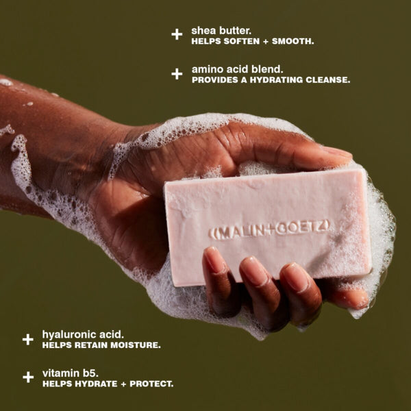 Hand holding a bar of soap with text about its ingredients on a green background