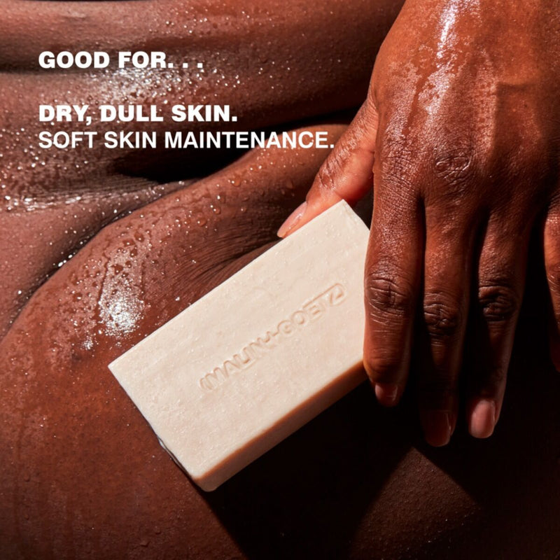 Bar of soap being held by a hand with text about skin care benefits on a brown background